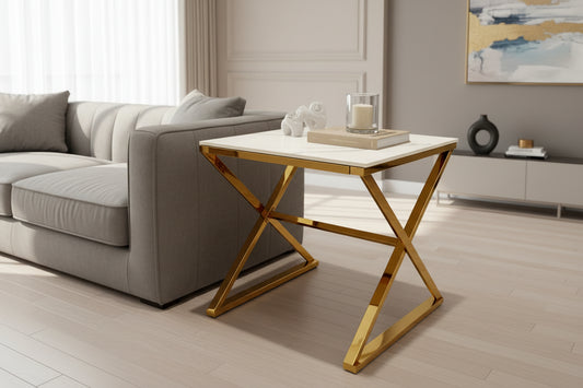 A modern living room showcases the Zion Gold Lamp Table with Polar White Sintered Top beside a gray sofa, topped with a glass candle, book, and white decorative elephant. Light wood floors and abstract art add the finishing touches.