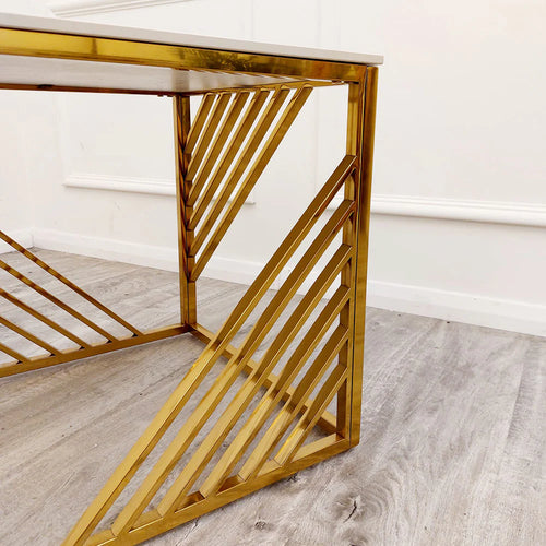 A modern desk with gold metal legs and a white tabletop is paired with the Azure Gold Lamp Table, featuring a Polar White Sintered Top, set on light wood flooring against a white wall.