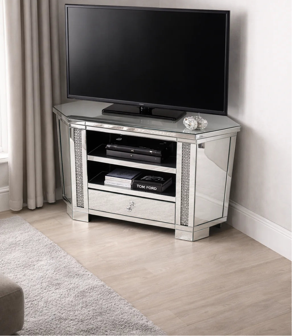 A flat-screen TV rests on the Roma Corner Mirrored TV Unit with a glass drawer and shelves for electronics, beside cream curtains and a beige carpet on light wood flooring—a stylish, space-saving TV solution.