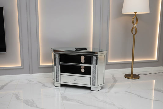 The Roma Corner Mirrored TV Unit features two open shelves, a bottom drawer, reflective surfaces, decorative side accents, and sparkling crushed diamond details for added glamour.