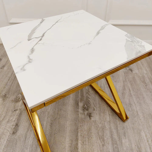 The Zion Gold Lamp Table with Polar White Sintered Top features a square white surface with grey veining, gold geometric metal legs, and is shown on a light wood floor.